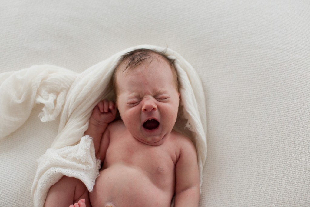 The art of the unposed newborn baby yawning in white wrap during newborn session