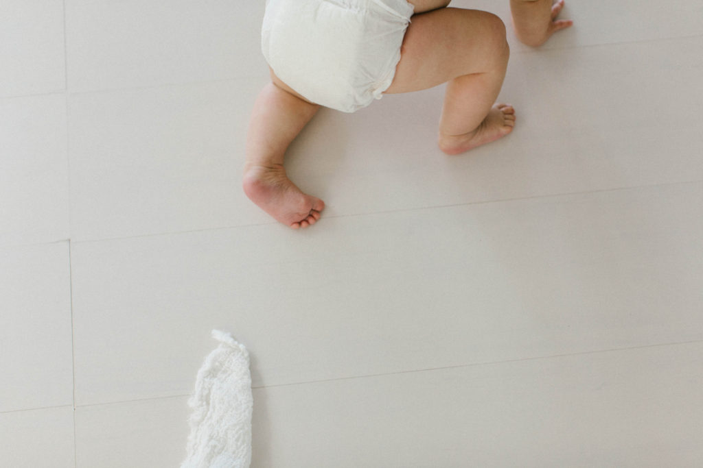Authentic newborn and baby photography of a baby crawling in white diaper on white floor 