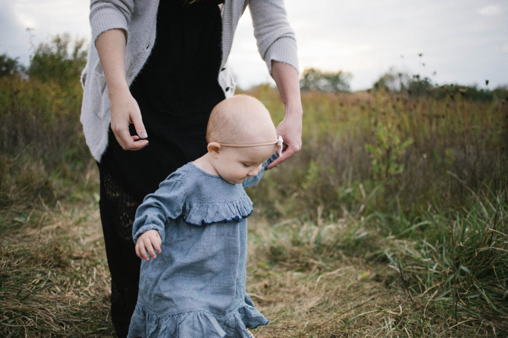 Large family sessions with Elle Baker Photography near Chicago. A young baby girl in a field learning how to walk 