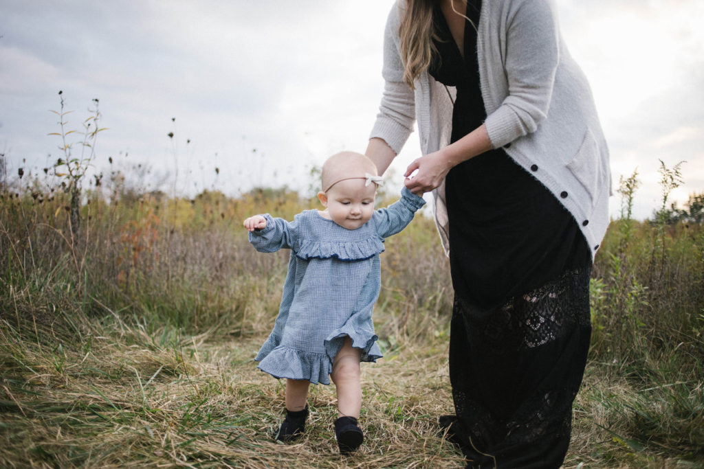 Large family sessions with Elle Baker Photography near Chicago. A young baby girl in a field learning how to walk 