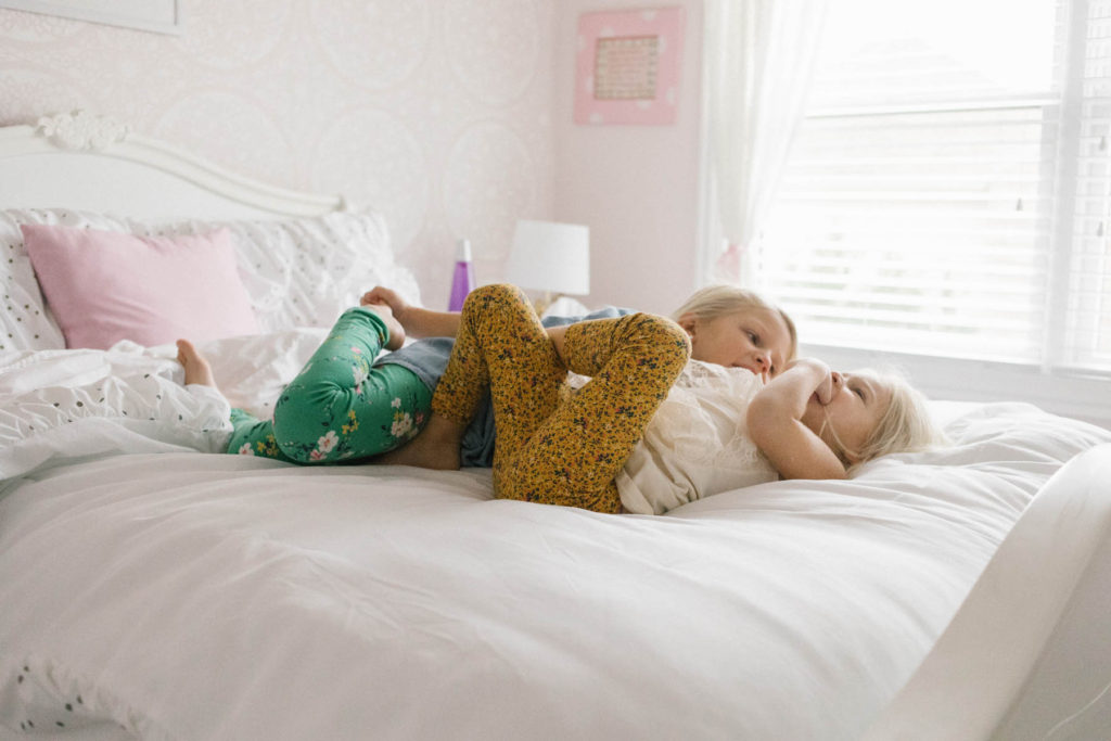 Chicago newborn and family lifestyle photographer, Elle Baker Photography, sibling sisters playing on bed during home session