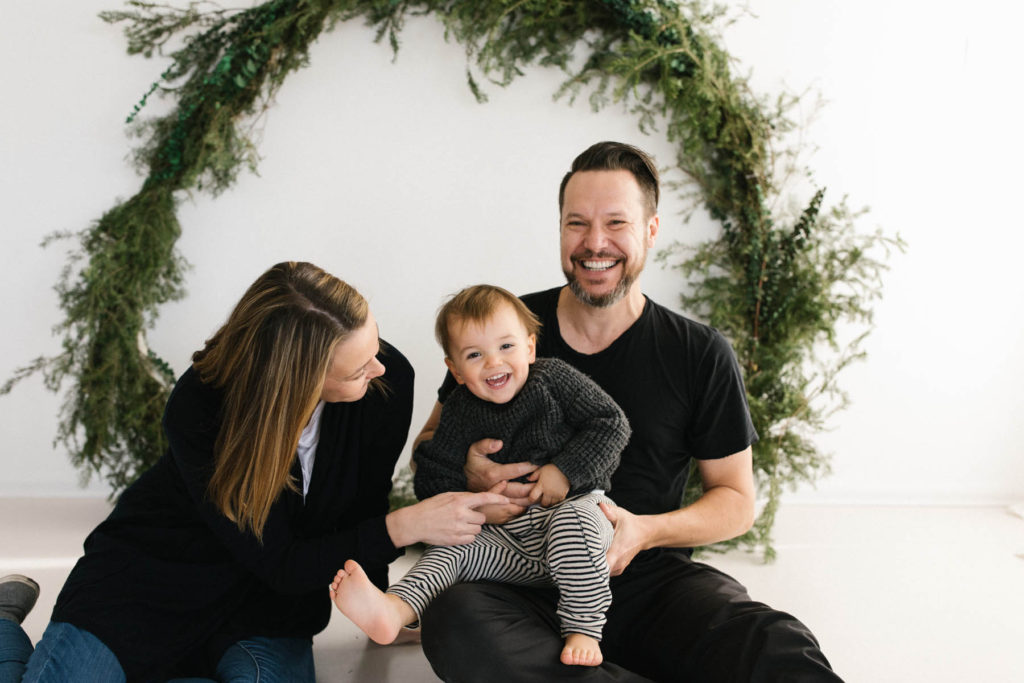 Homer Glen, IL Holiday Mini Sessions, Photo by Elle Baker Photography, family of three posing in front of a wreath themed Christmas session