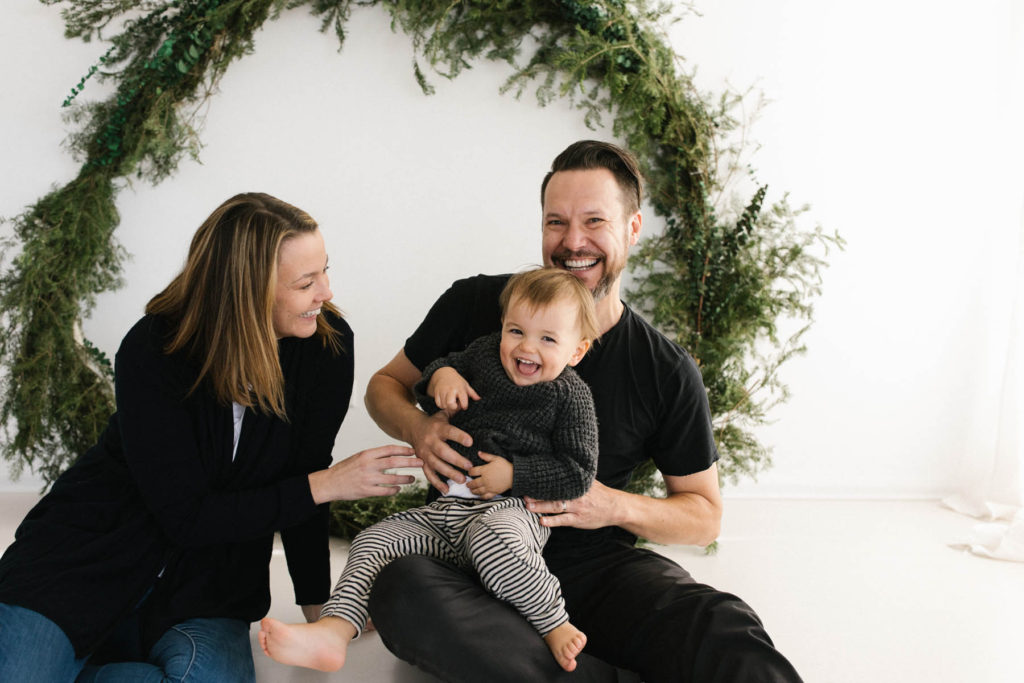 Homer Glen, IL Holiday Mini Sessions, Photo by Elle Baker Photography, family of three posing in front of a wreath themed Christmas session