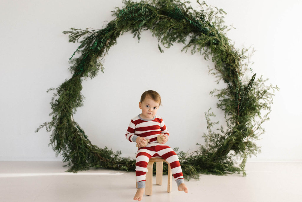 Homer Glen, IL Holiday Mini Sessions, Photo by Elle Baker Photography, boy posing with ornaments and a large wreath during Christmas session