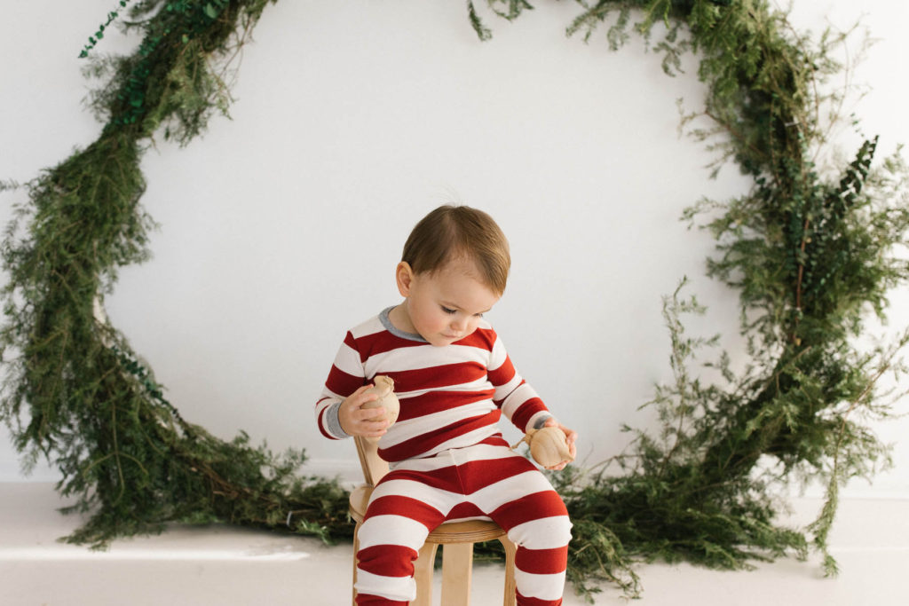 Homer Glen, IL Holiday Mini Sessions, Photo by Elle Baker Photography, boy posing with ornaments and a large wreath during Christmas session