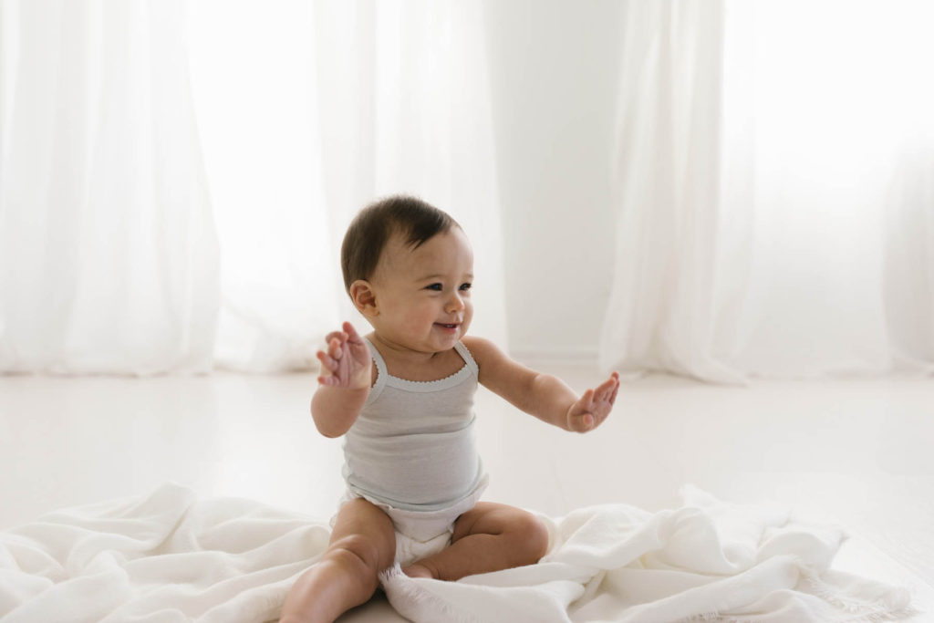 simple and natural baby session, Photo by Elle Baker Photography, baby girl in white studio space in Chicago smiling and waving her hands
