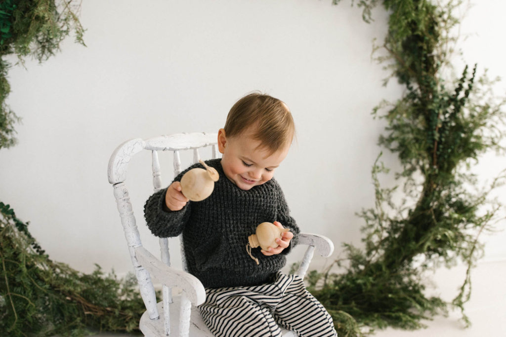 Homer Glen, IL Holiday Mini Sessions, Photo by Elle Baker Photography, boy playing with wooden ornaments and posing with large wreath during Christmas session