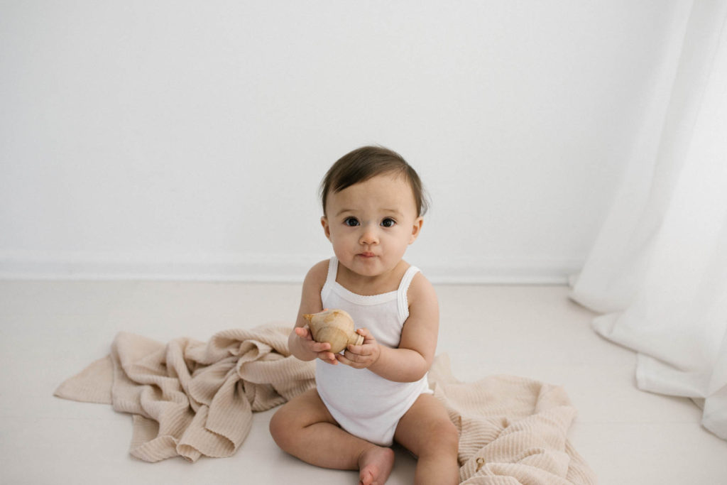 Simple and natural baby session, Photo by Elle Baker Photography, baby girl in white studio space in Chicago playing with a wooden ornament teether