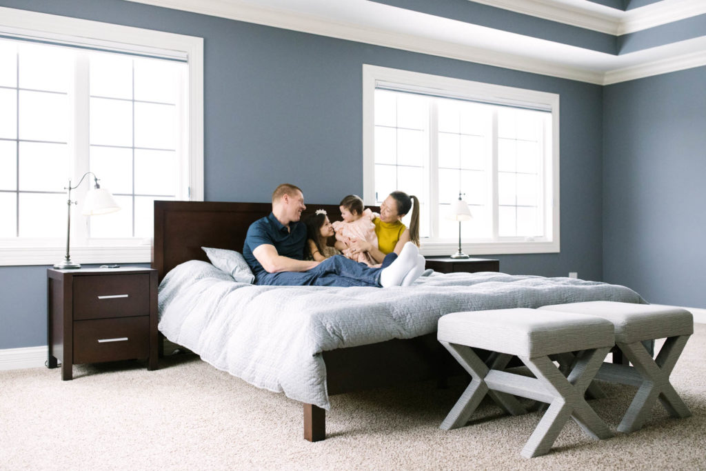 Naperville lifestyle family photographer Laurie Baker captures family of four on large bed cuddling and laughing