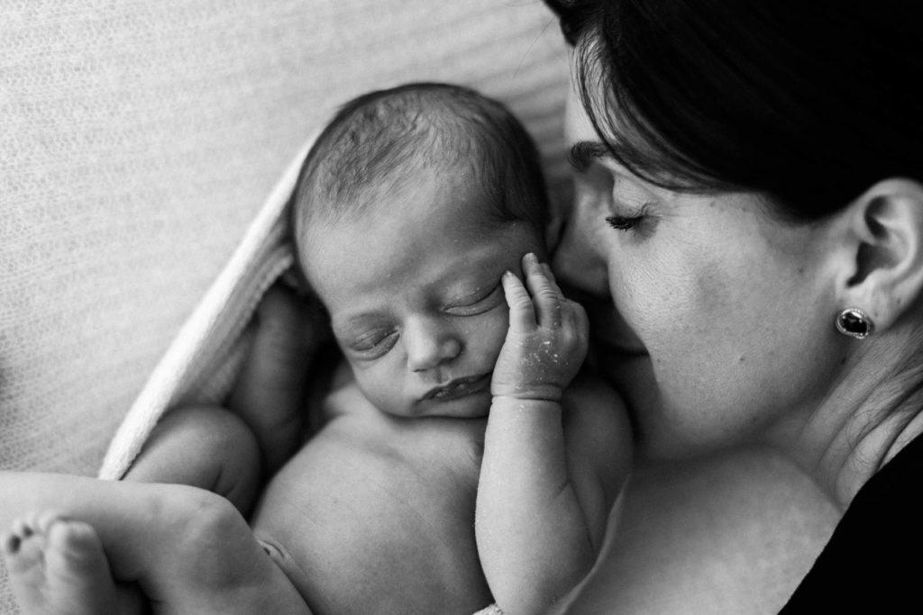 black and white image of smiling mother sleeping next to a brand new baby curled in a natural wrap 