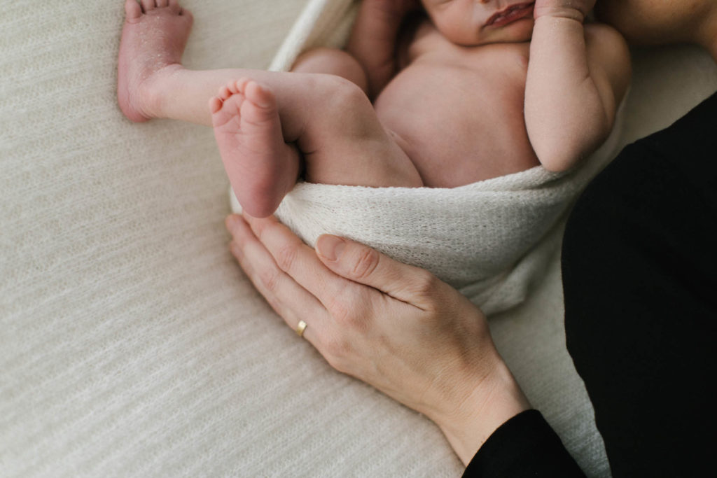 Detail shot of mother holding newborn baby on a bed at a Chicago newborn photography studio