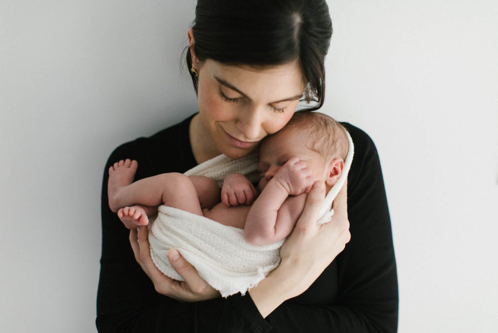 new mom holding newborn boy curled in a neutral organic cloth in a white studio