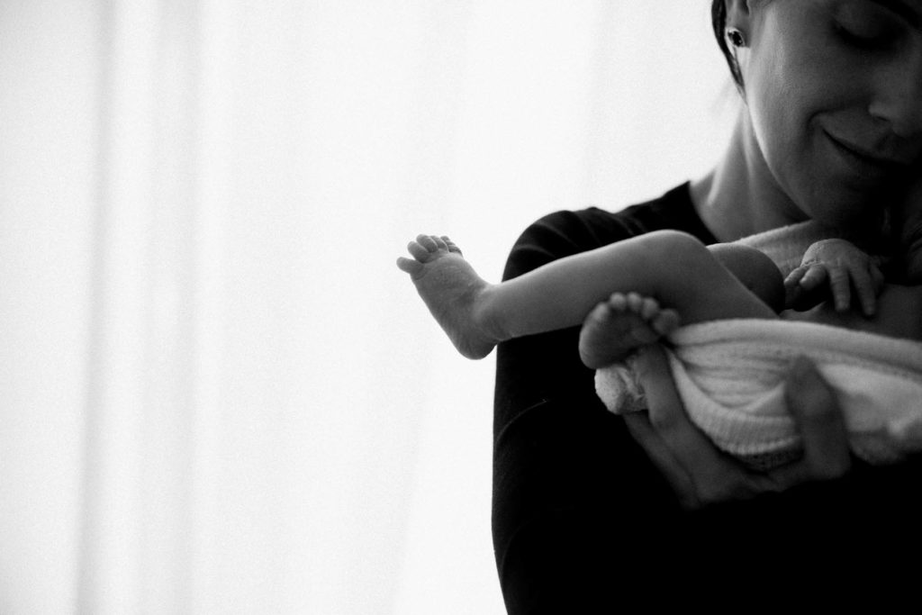 black and white image of a new mother holding her newborn boy and he stretches his foot and toes