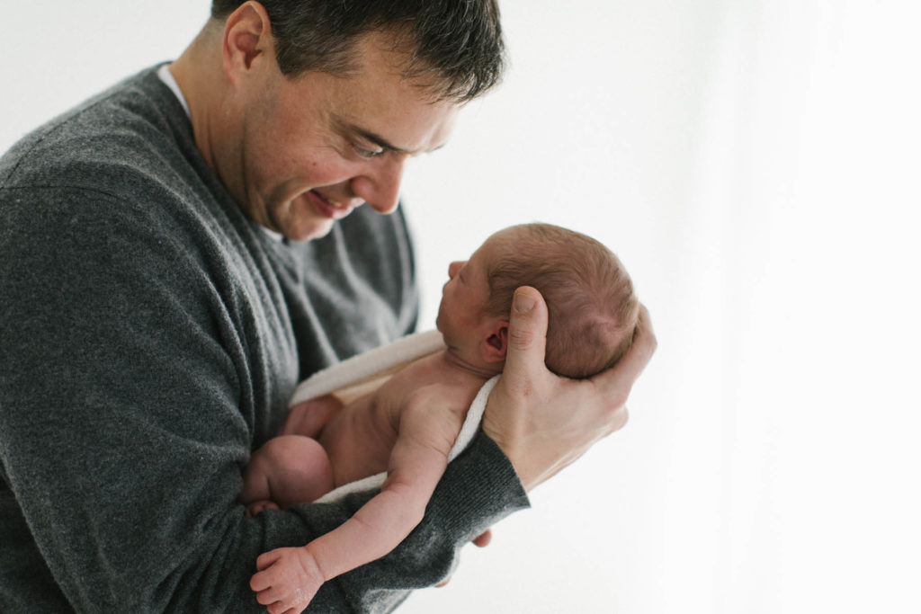New dad holding newborn baby in his arms in a natural light studio