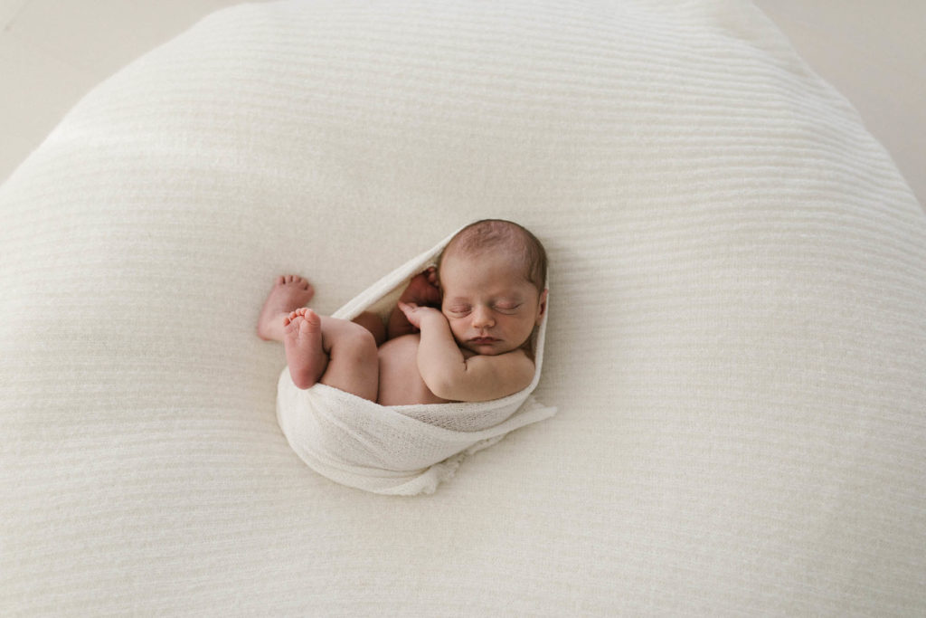 tiny newborn baby wrapped tightly in a neutral organic wrap and curled into a fetal position