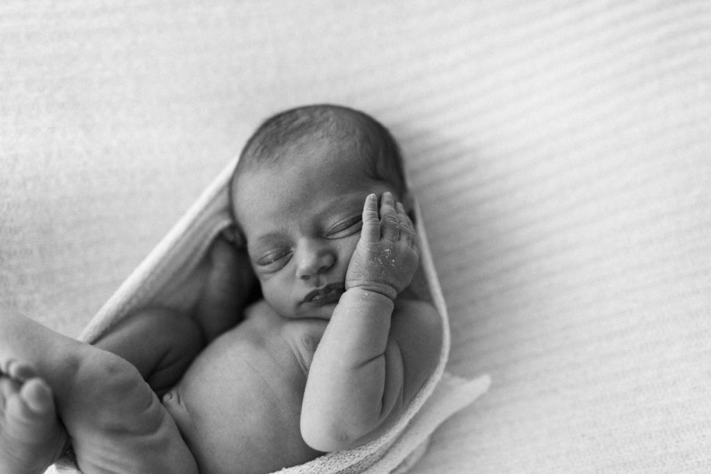 black and white image of newborn baby with his little hand resting on his cheek 