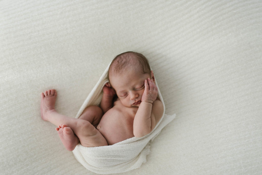 simple newborn set up with white blanket and newborn baby wrapped in an ivory scarf
