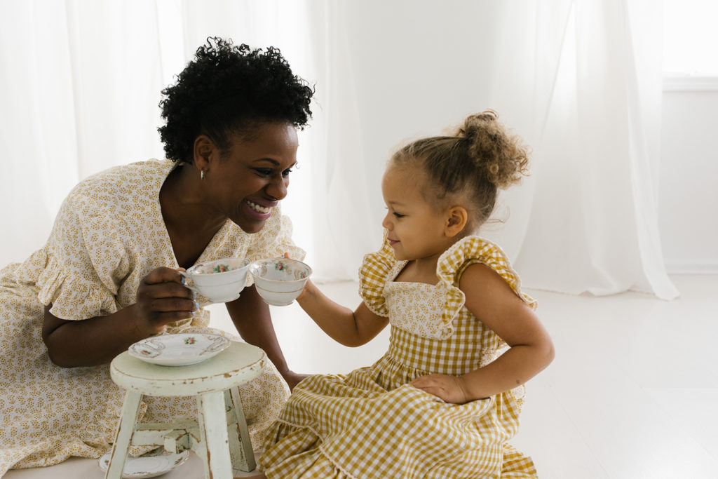 woman playing tea party with her daughter wearing yellow matching dresses 