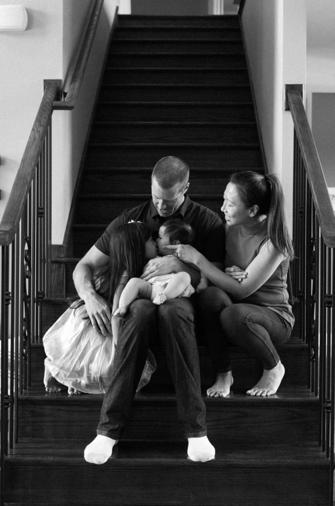 family of four sitting on stairs cuddling and kissing
