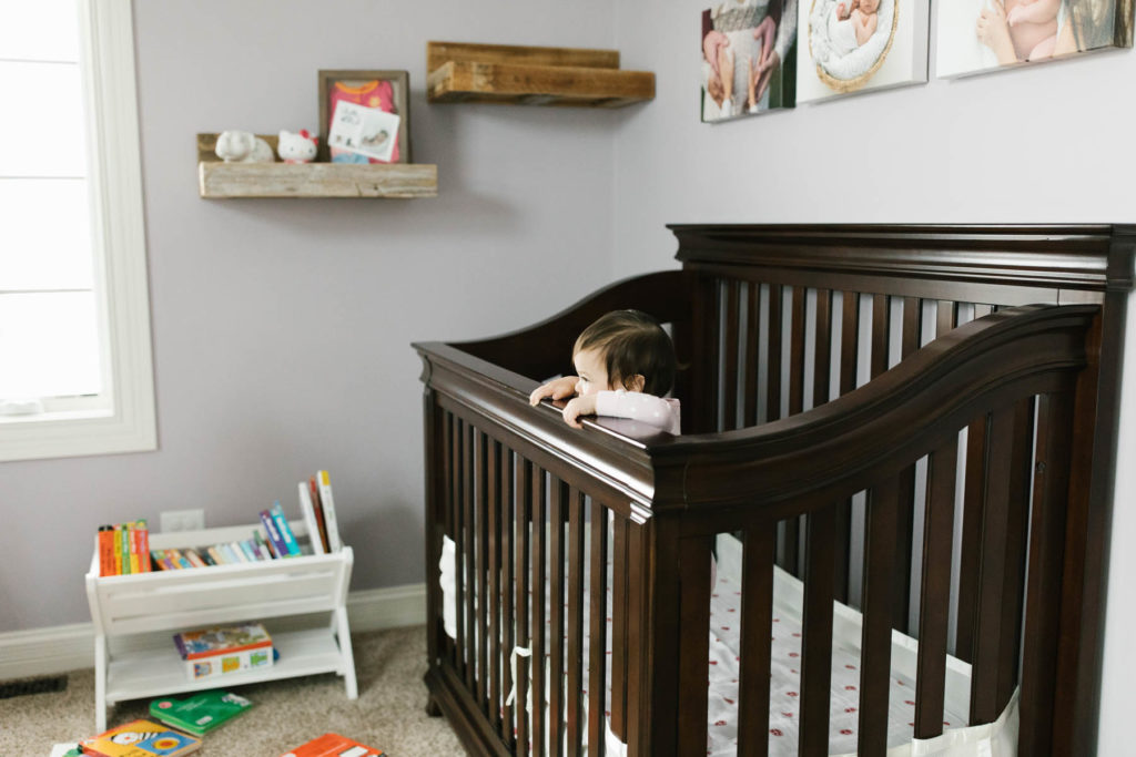 baby girl chewing on her brown wooden crib 