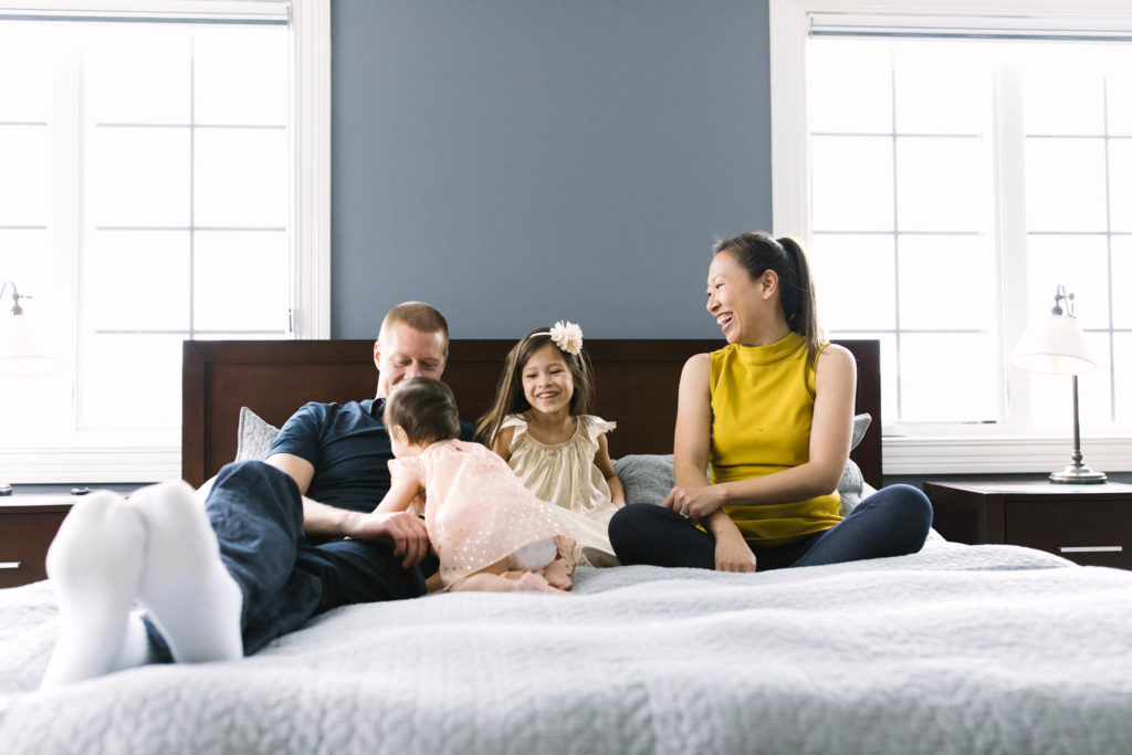 funny family of four playing around on a bed in their master bedroom