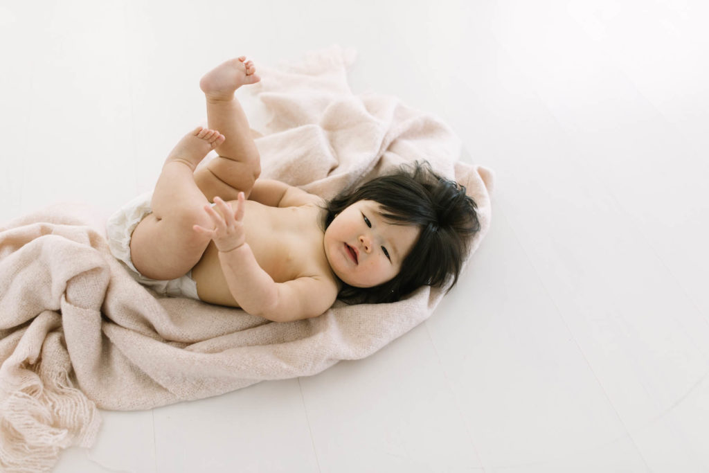 baby girl lays on a blanket while kicking up her feet, posing idea for milestone session 