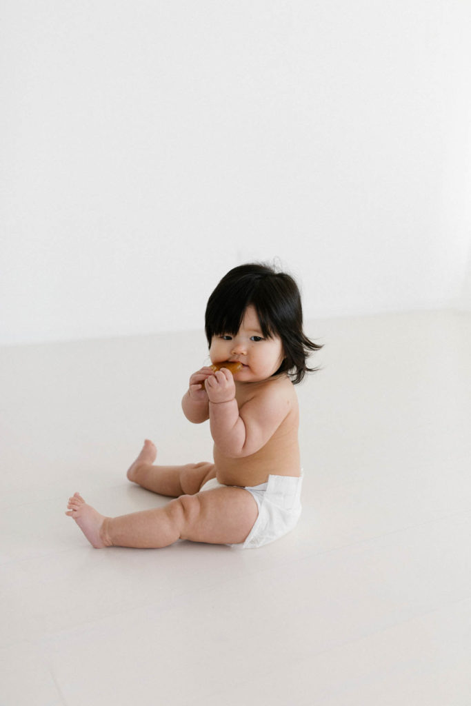 baby girl chews on toy during her milestone session in a white studio 
