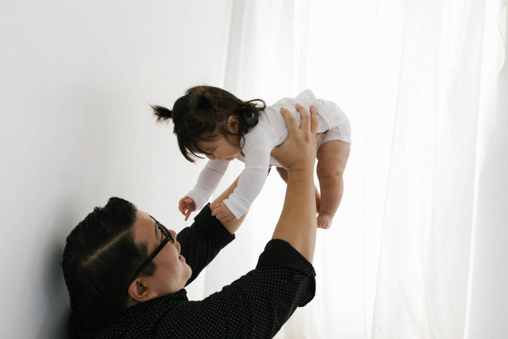 dad holding baby girl wearing a white shirt in the air smiling 
