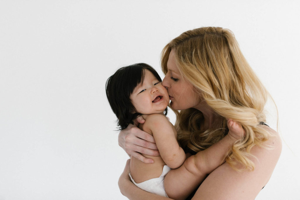 mother with light hair kisses baby girl with dark hair 
