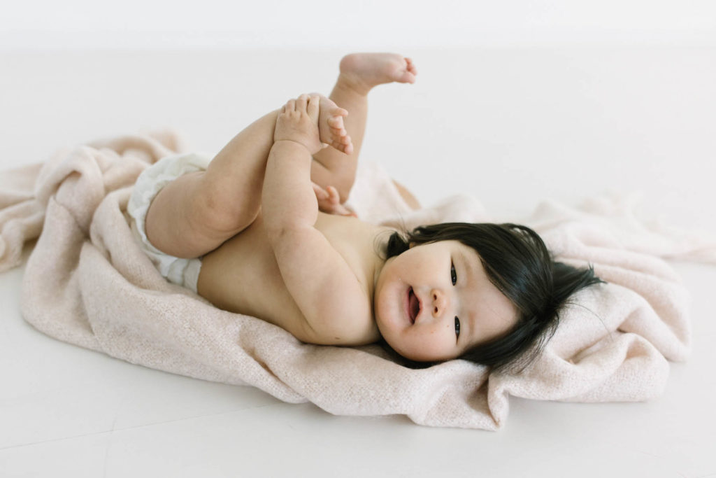 six month milestone session with a baby girl laying on a pink blanket holding her toes