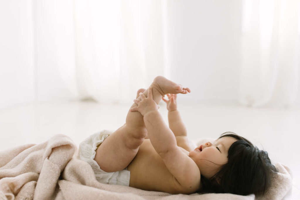 baby discovers her toes laying on a blanket in a white studio