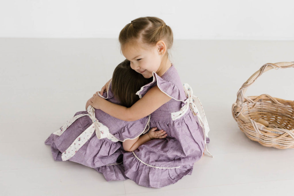 two toddler girls in lilac matching dresses hug each other 