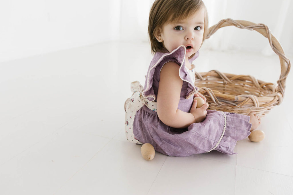 two year old girl looks at camera holding a wooden egg and easter basket