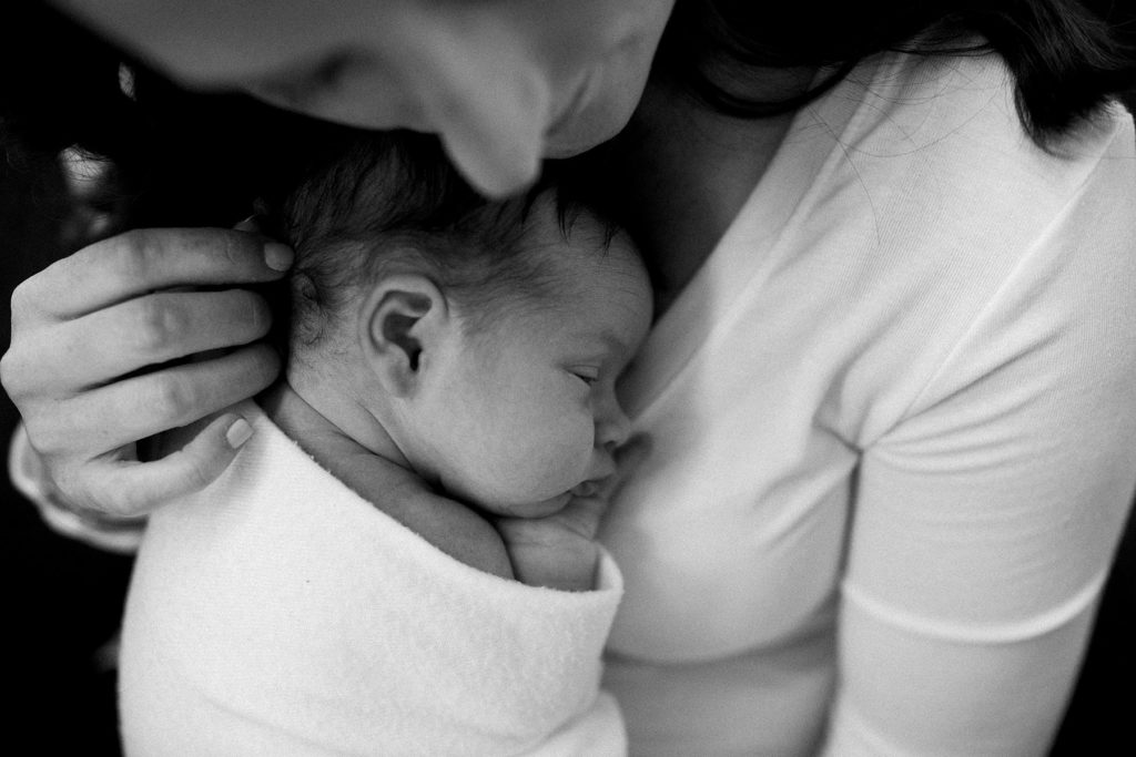 Downers Grove newborn photographer Laurie Baker photographs a motherhood image of a mother holding her newborn baby girl and stroking her hair