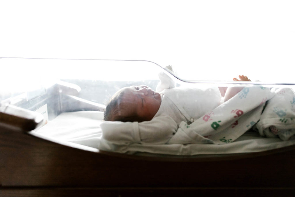 newborn baby laying in clear bassinet in hospital during newborn session with Laurie Baker 