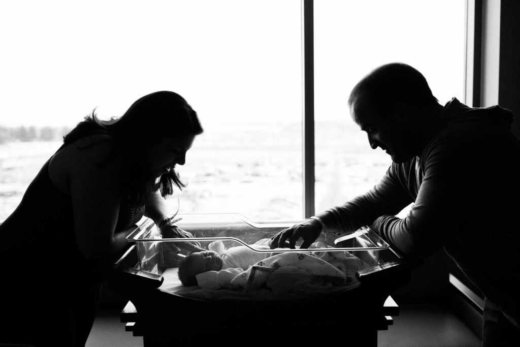 black and white images of parents looking at newborn baby in bassinet