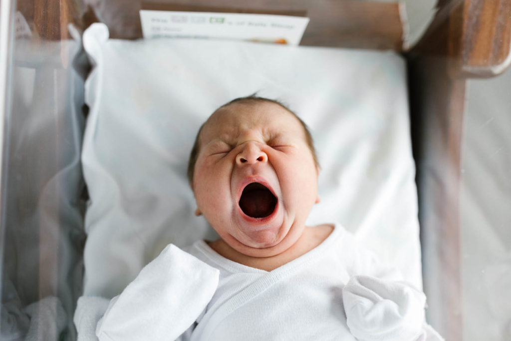 A newborn yawning in a hospital bassinet during a Fresh 48 session with Elle Baker Photography 