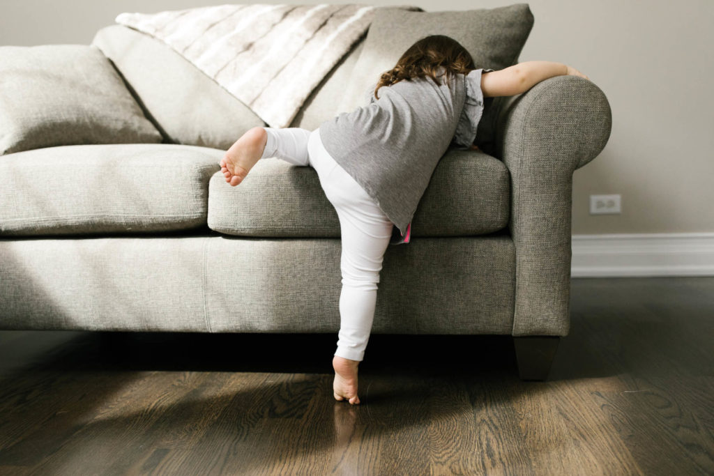 little girl climbs on a couch during lifestyle session