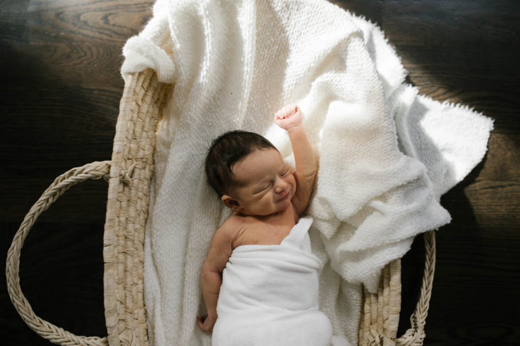 Elle Baker Photography captures a newborn baby stretching in a Moses basket 
