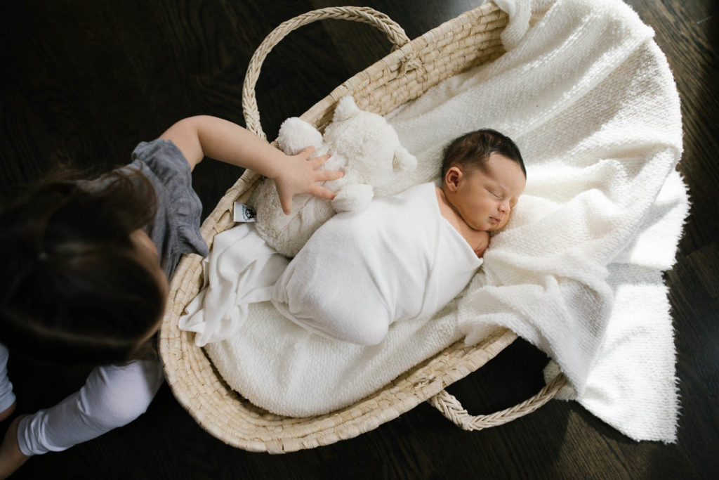 Elle Baker Photography captures a big sister and newborn baby in a Moses basket 