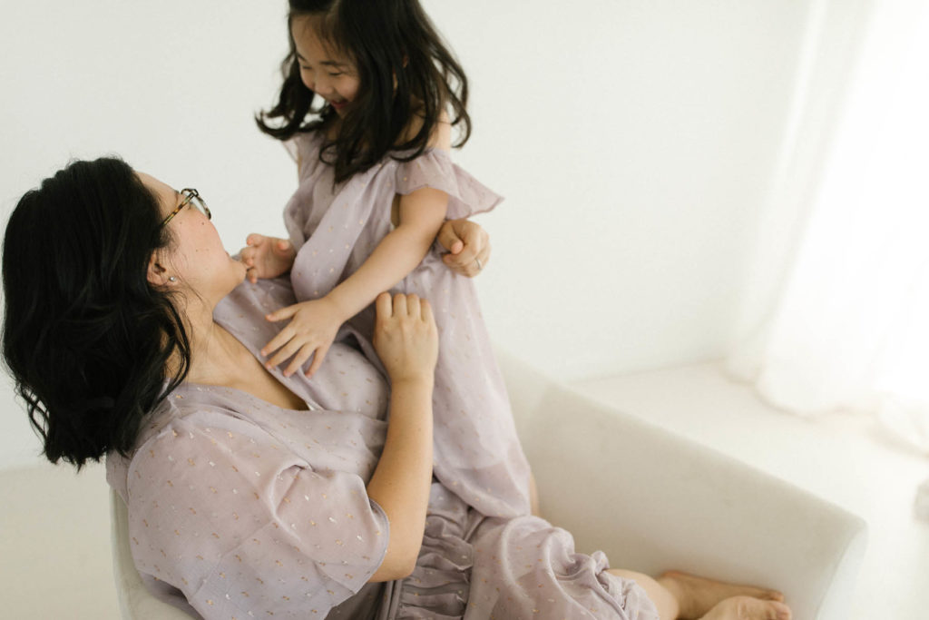 little girl tickles her mother wearing dresses by Ele Story