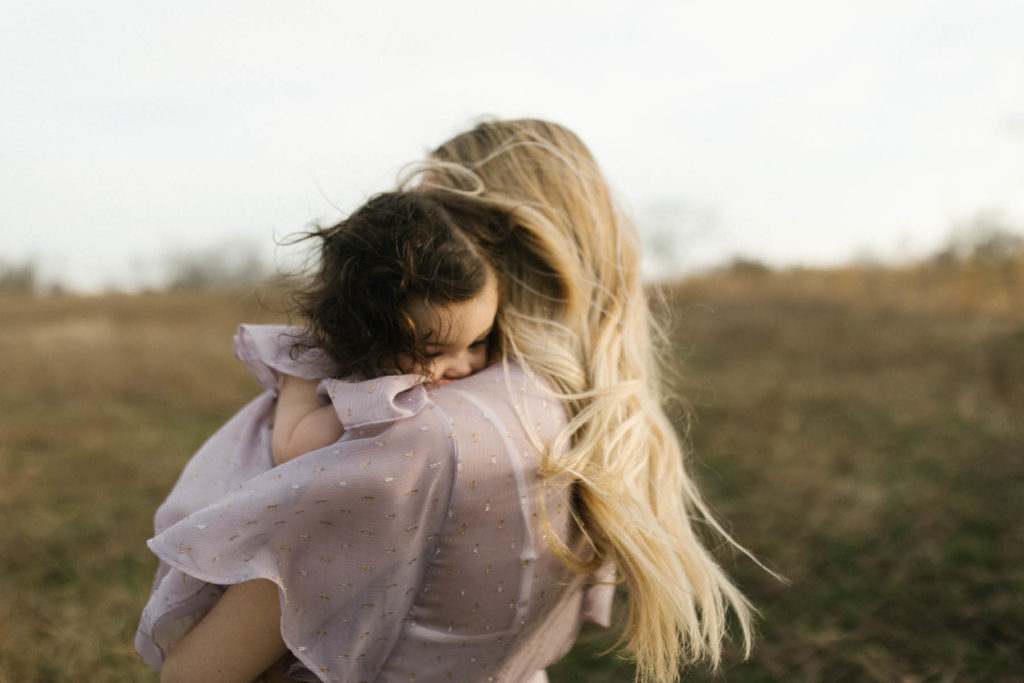 mother holding daughter while their hair blows in the wind during sunset session, photo taken by Elle Baker Photography 