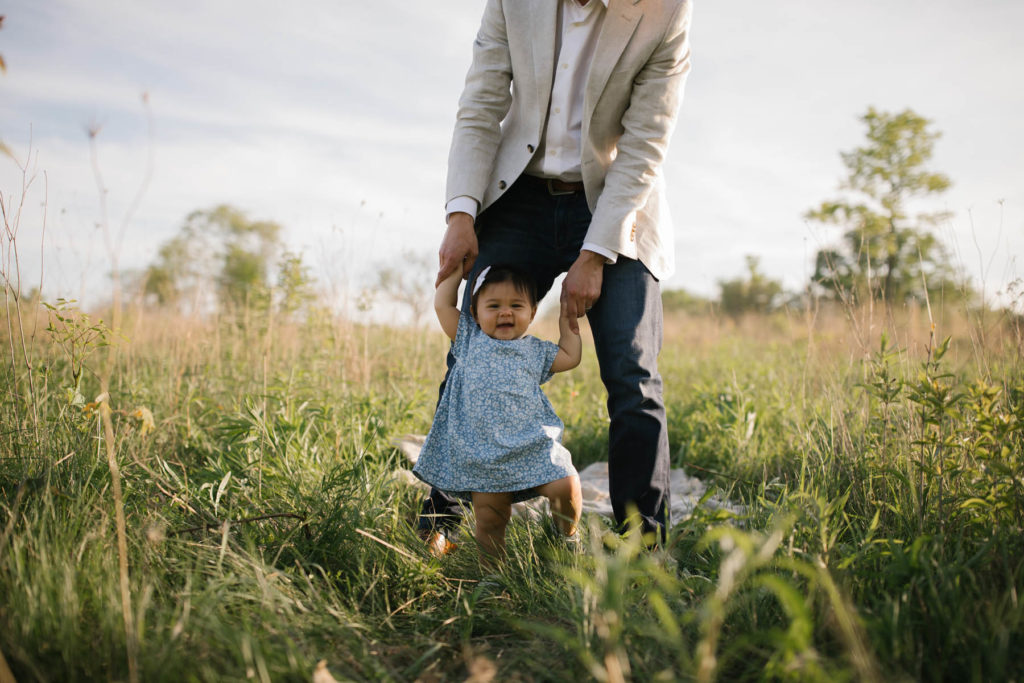 baby girl smiling as her father helps her walk, photographed by Elle Baker Photography