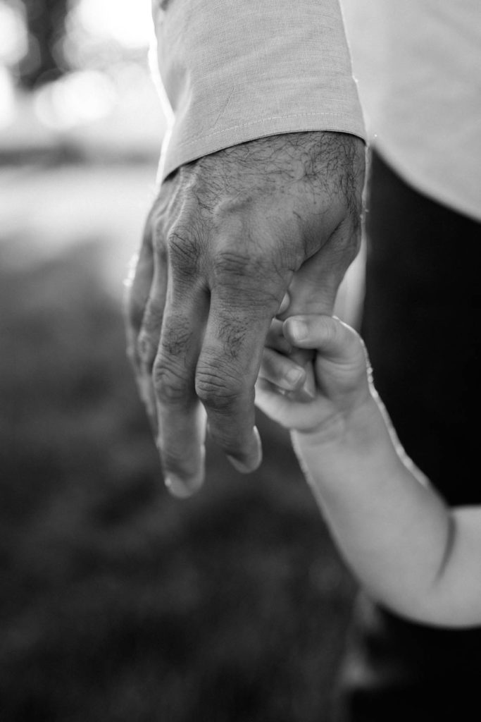 black and white image of a toddler holding her father's hand