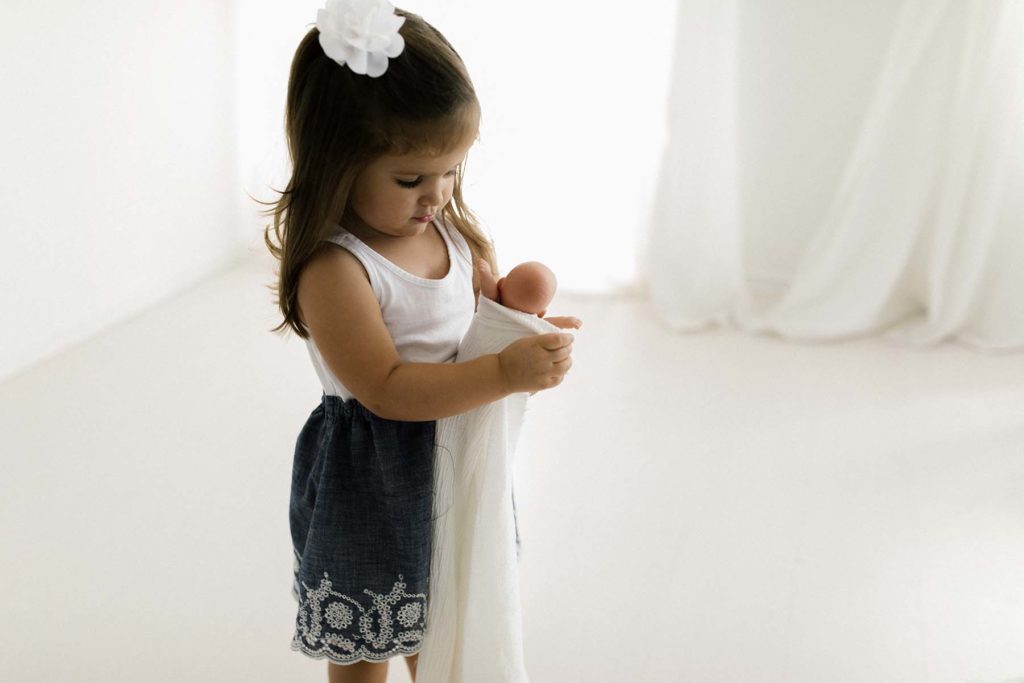 toddler girl wrapping baby doll during photo session with Elle Baker Photography 