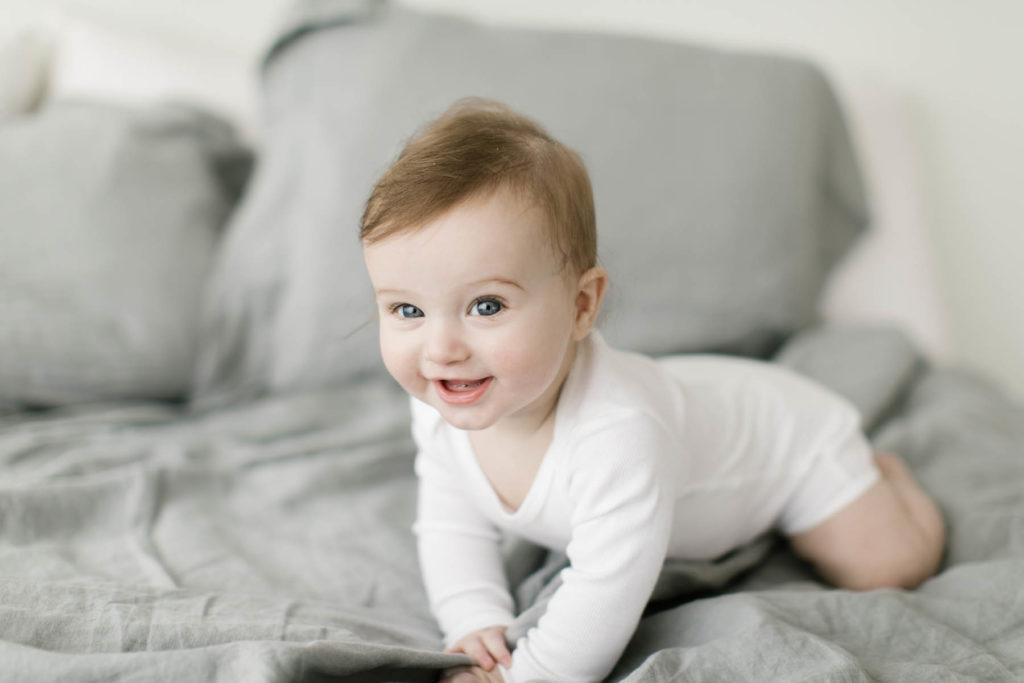 baby boy crawls on bed in a white onsie during six month milestone session 