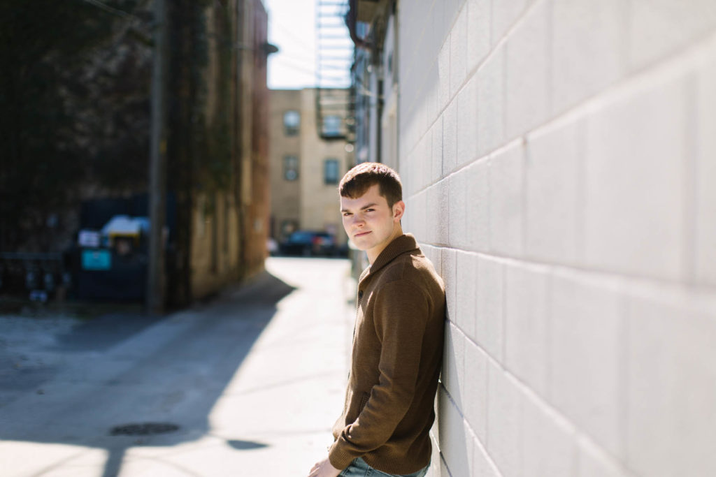 guy stands in an alley during senior portrait session 