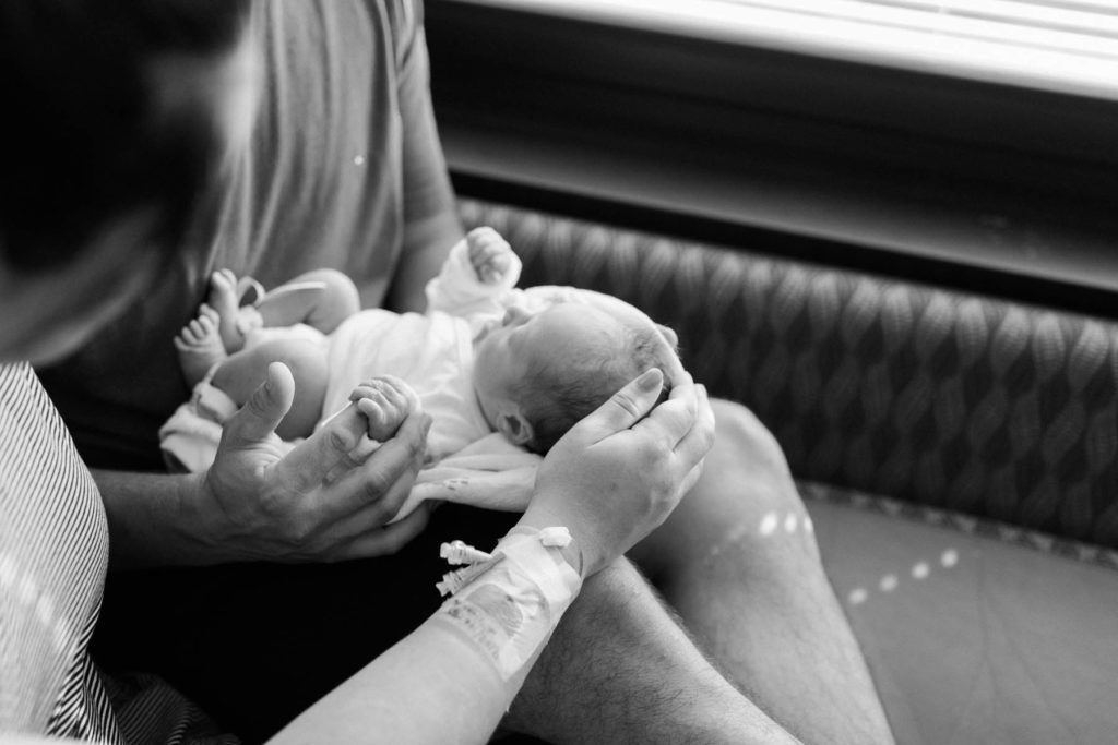 black and white image of mother stroking her baby's head and dad holding his hand