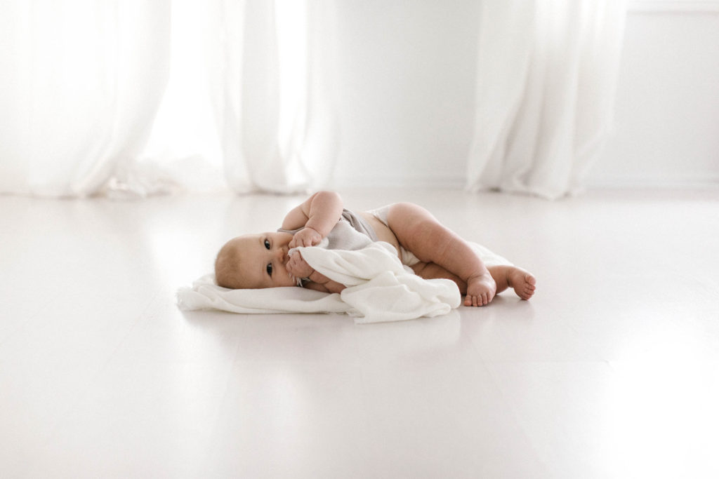 Belly to baby package offered by Elle Baker Photography image of baby laying with white blanket in white studio