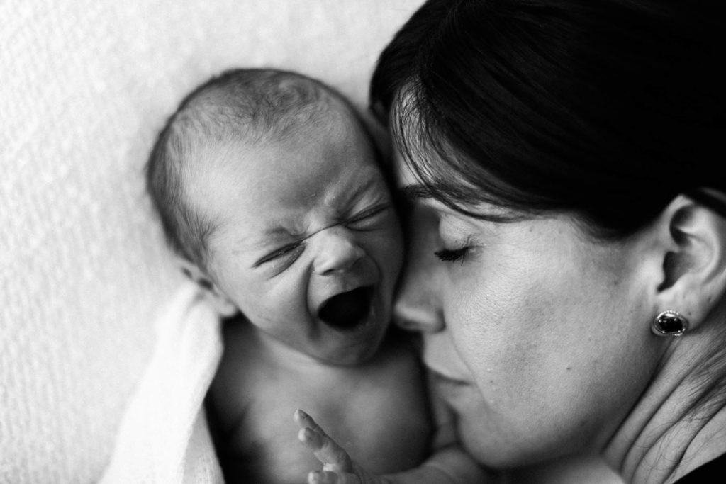 Black and white image of new mother sleeping next to her yawning newborn baby boy, simple white set up in Laurie Baker's Chicago newborn photography studio